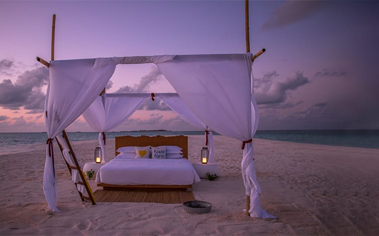 A bed on white sand besides sparking waters of the Indian Ocean